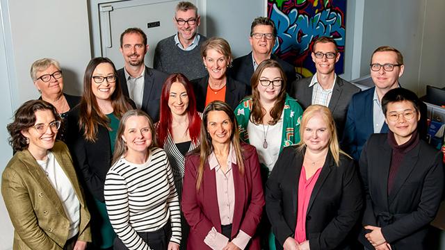 A group of about 15 people in smart casual dress assembled formally and smiling into camera