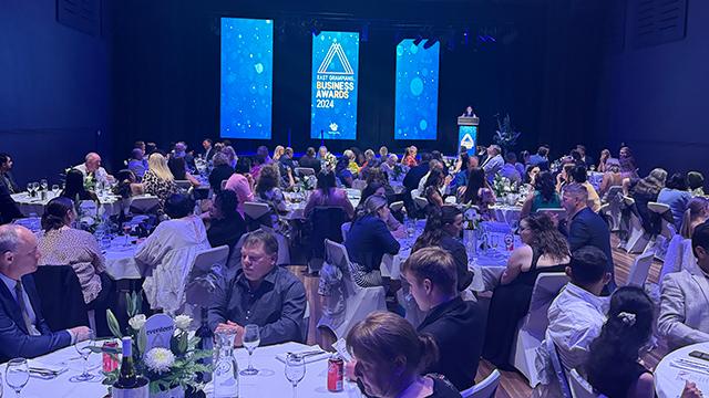 Large audience seated at dinner tables inside decorated auditorium