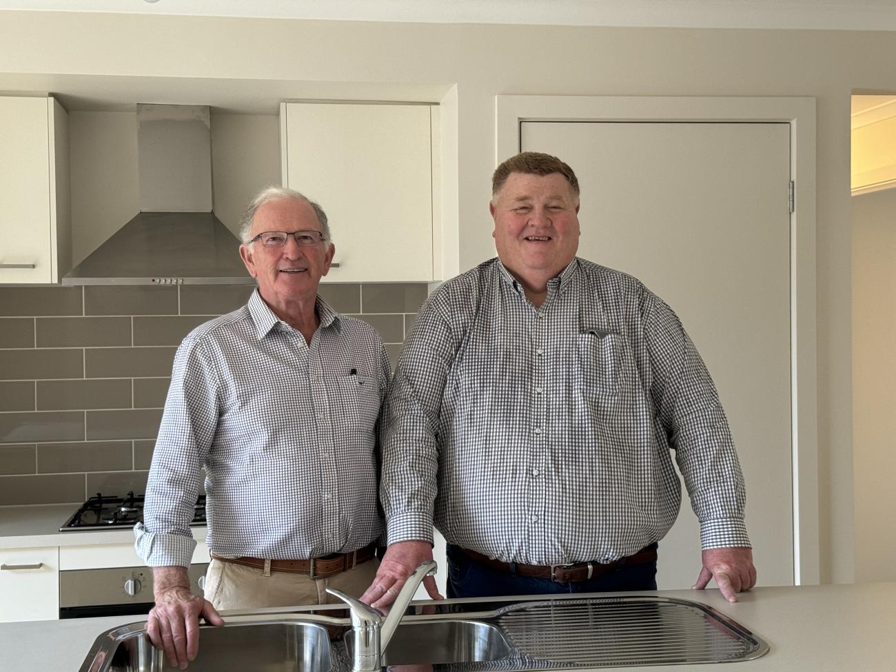 Two men smiling and standing inside the kitchen of a new house