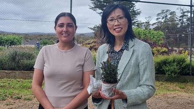 Two women standing outside and smiling with one holding a little potplant