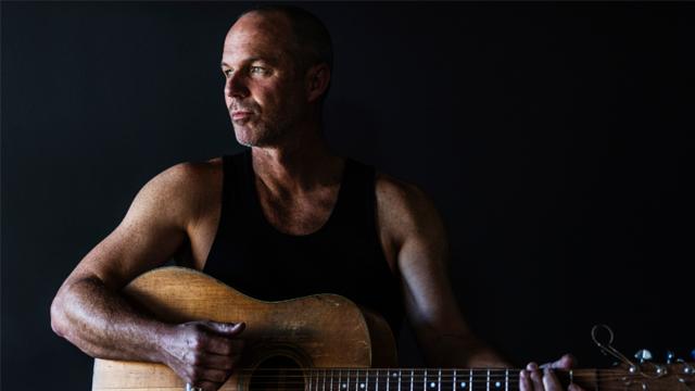 Man holding a guitar and looking moodily off to the left