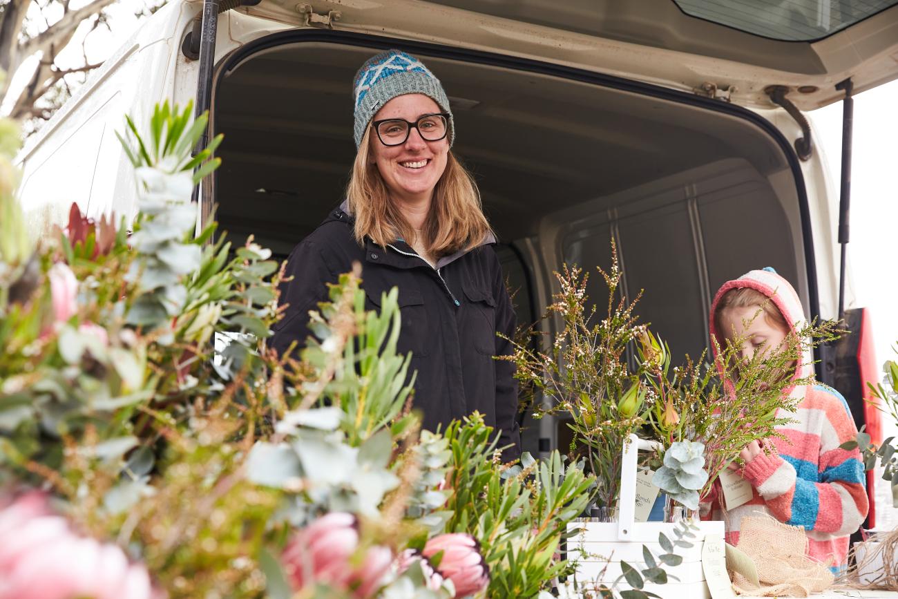 Woman wearing a beanie, standing behind a table of flower arrangements