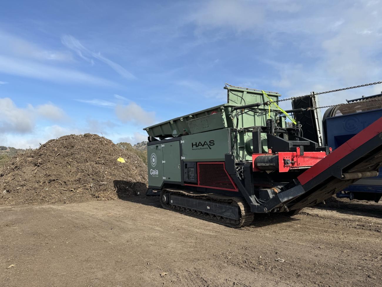 Long shot of a large pile of compost, in front of which is a mobile shredding machine