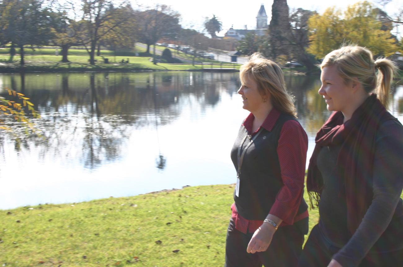 Two people walking alongside Alexandra Lake on a sunny morning