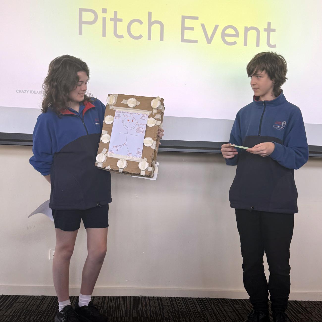 Two high school students standing up and speaking to an audience, one holding an explanatory poster 