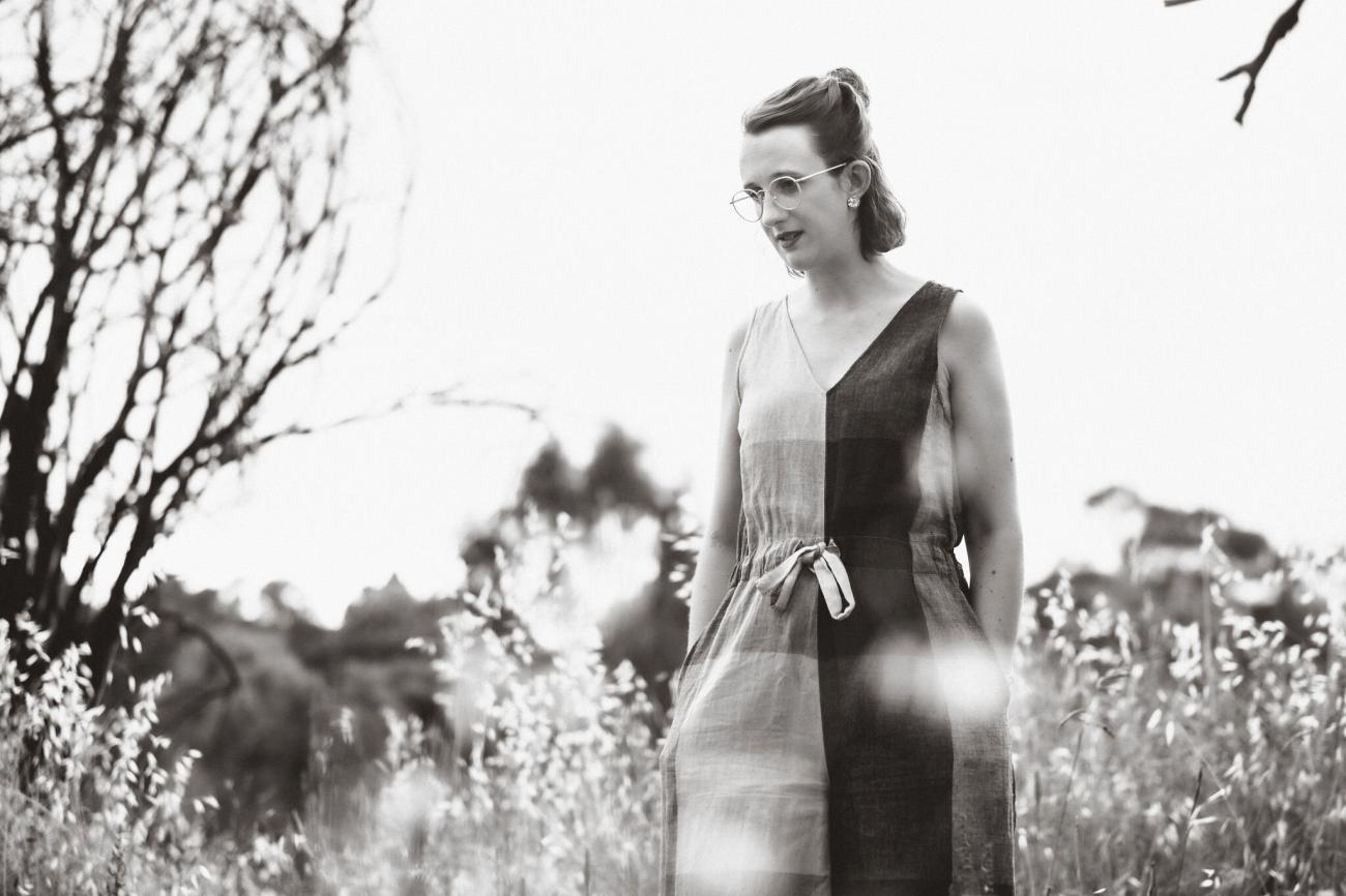 Black and white image of young woman walking through grassy parkland