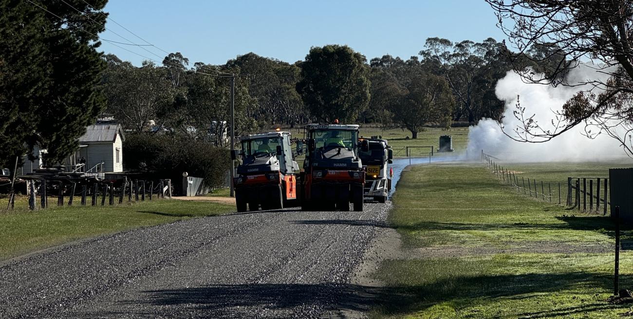 Roadworks vehicles driving along a freshly-sealed rural road