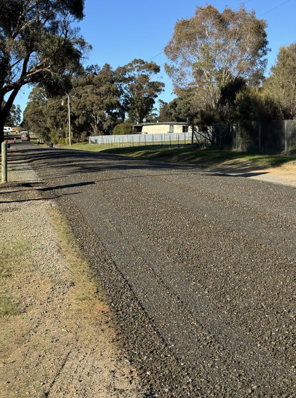 Freshly-sealed rural road with sunshine in sky