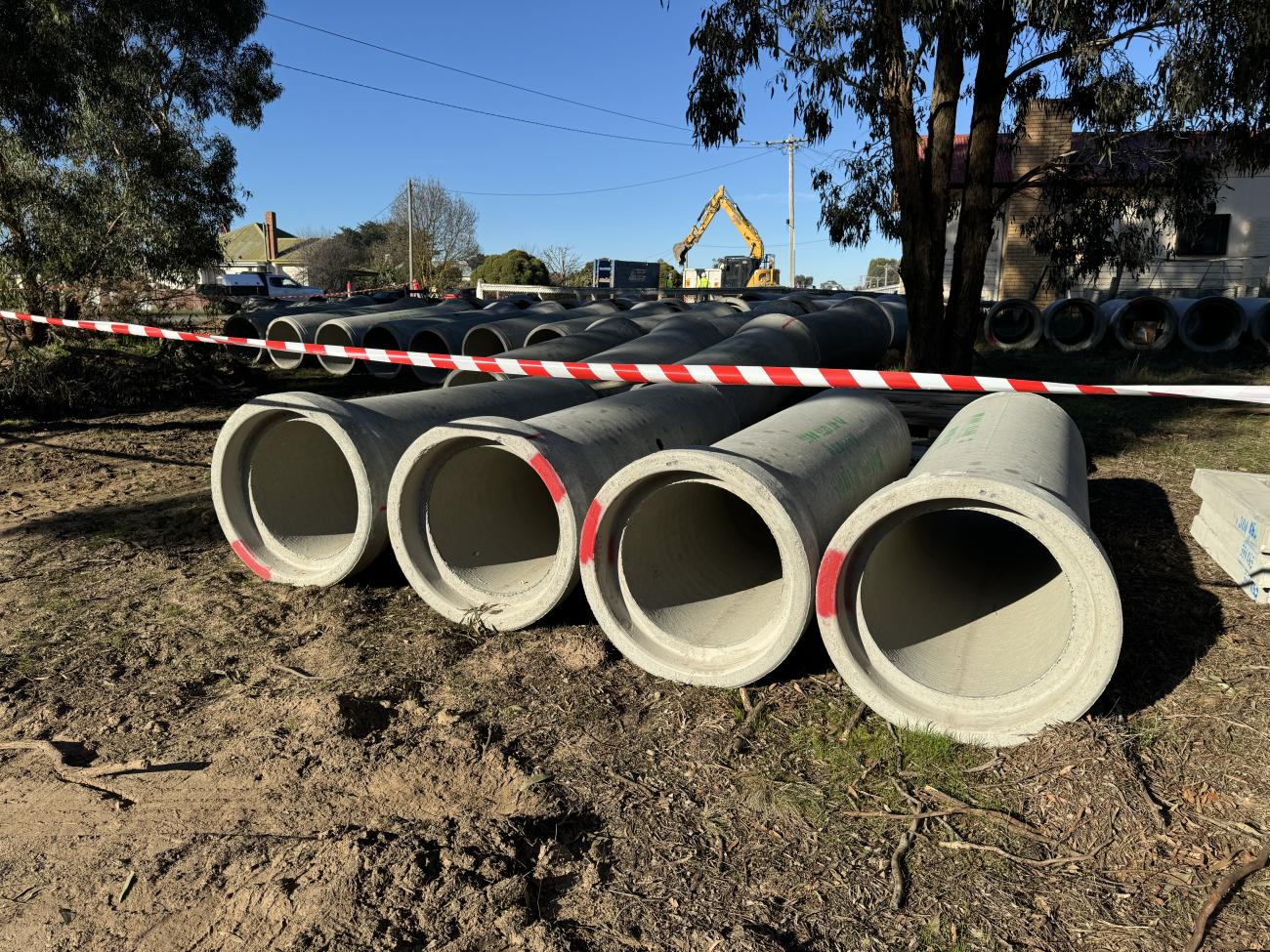 Large diameter concrete pipes laid in a row next to a freshly-dug roadside ditch