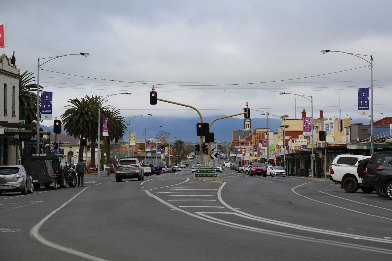 A small town's main street, with cars stopped at traffic lights and mist over the mountains in the distance