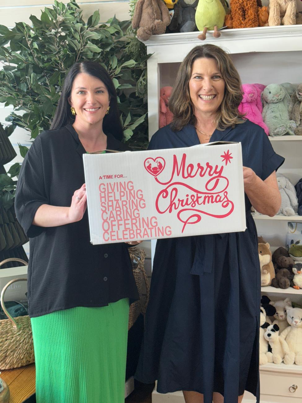 Two women smiling and holding a carboard box which says Merry Christmas on it