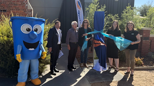 A large foam mascot of a bucket and a group of smiling people unveiling a public drinking fountain