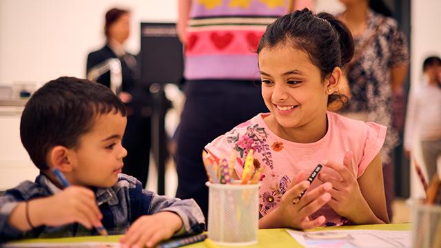 Two young children smiling while drawing with pencils