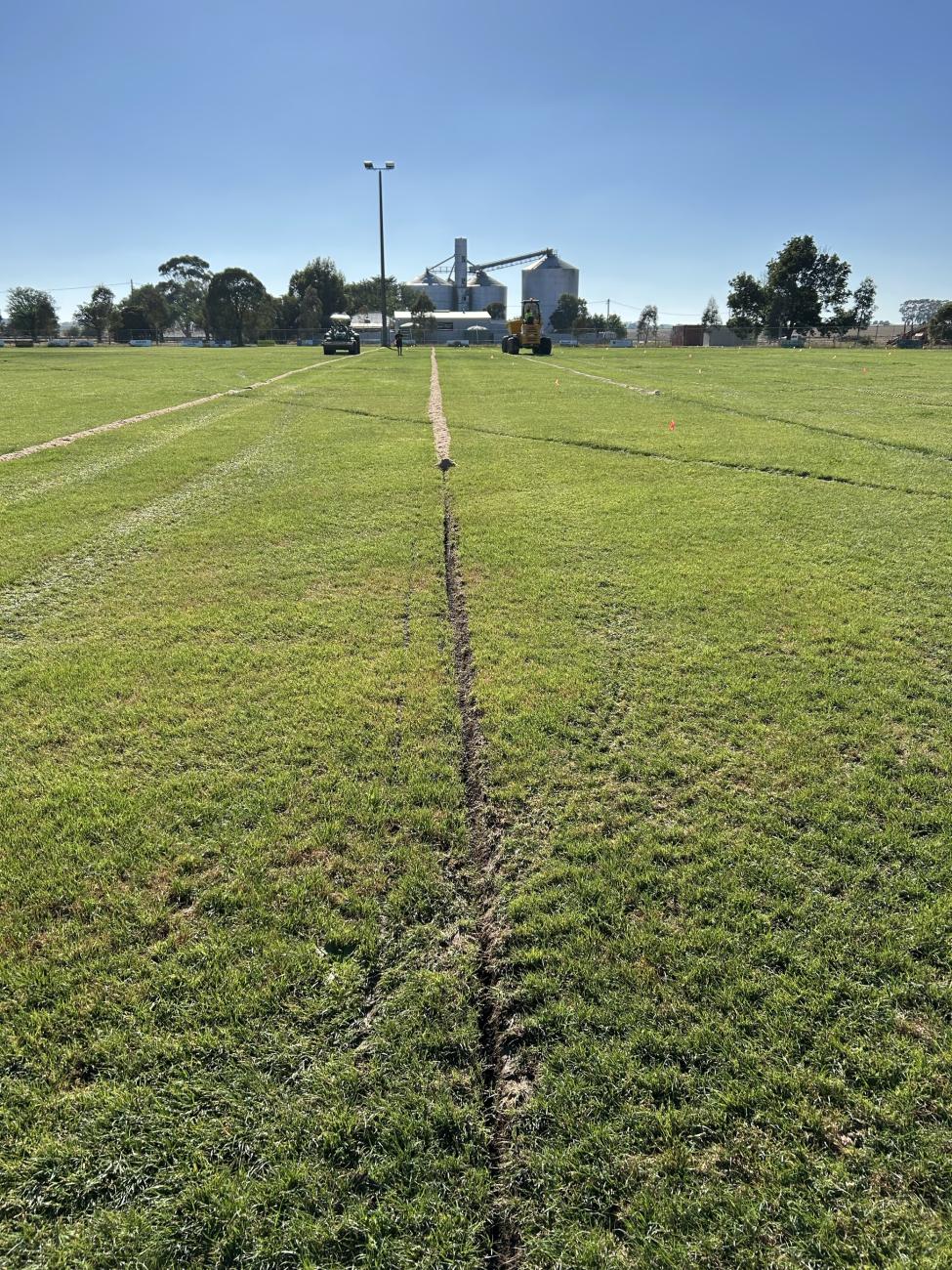 A large grassy field with a long, straight trench dug into it.