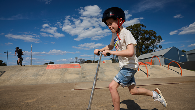 Young boy on a scooter with helmet on riding across a skate park bowl