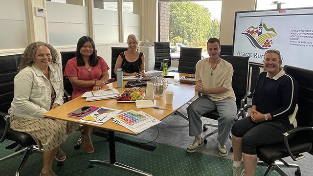 A group of people smiling while sitting around a table inside an office meeting room