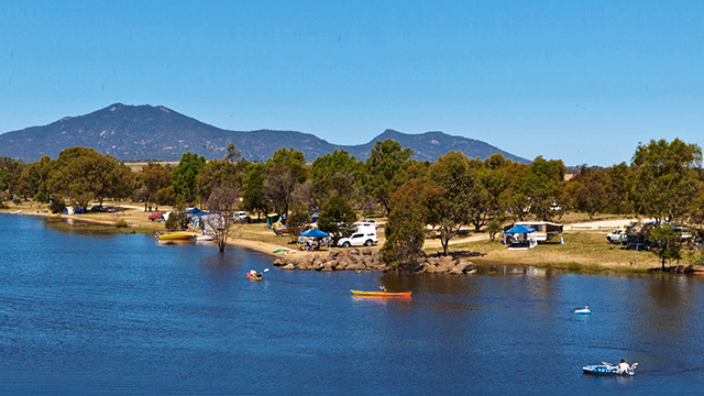 Lake with kayakers and campers around its banks underneath a bright blue summer sky