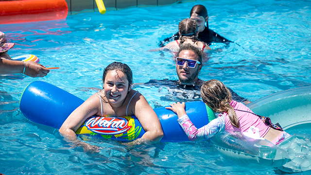 Several people in an outdoor pool in the sunshine with pool toys