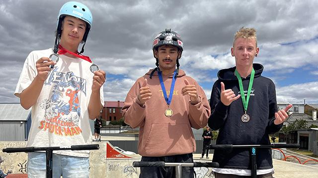 Three young men posing with medals at a skate park